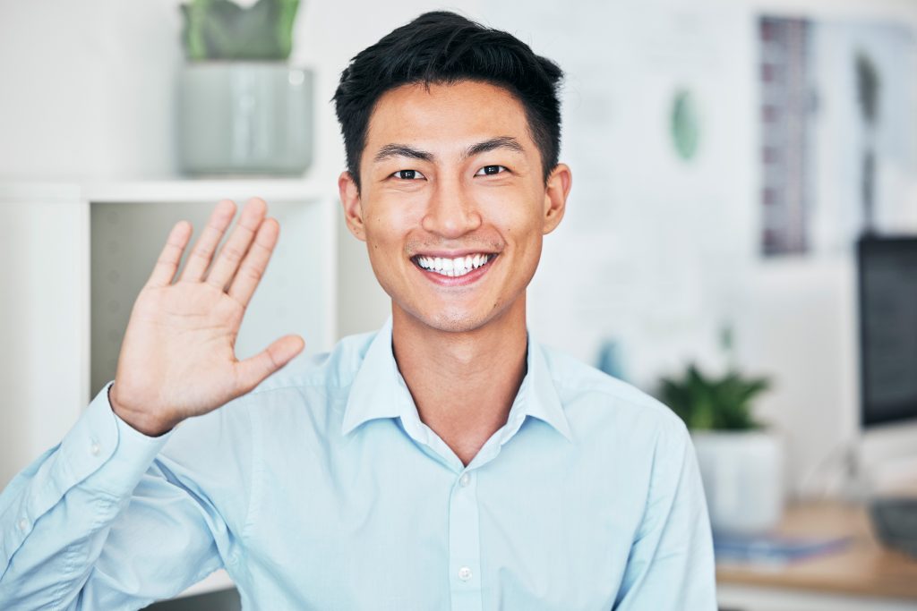 Happy business man greeting, waving and saying hello with hand gesture while smiling and looking fr.